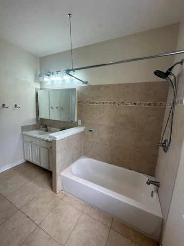 The Celebration bathroom before the upgrade, with a standard alcove tub, a curtain rod, and beige tile with a mosaic border
