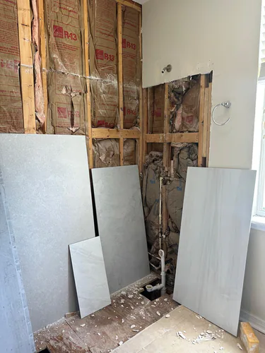 The tub alcove opened to the studs during construction, with the plumbing exposed and large format porcelain tile staged against the wall
