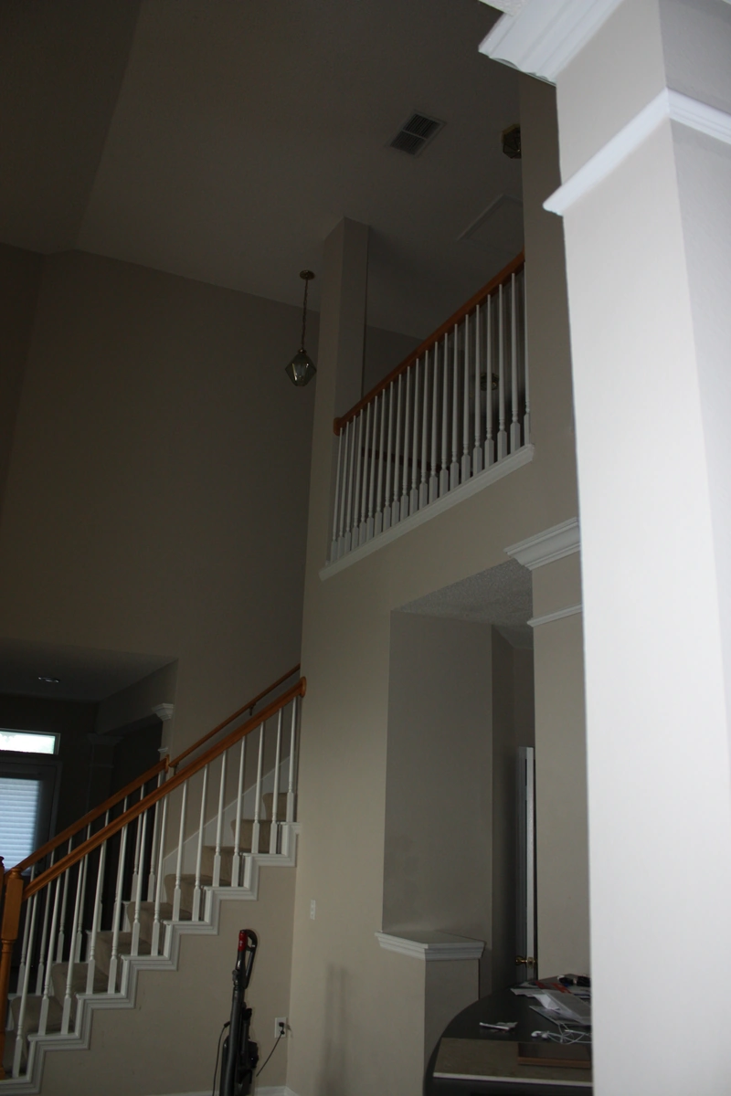 Celebration entry and stairway before remodeling, with beige two story walls, an oak and white spindle railing, and a small dated pendant light