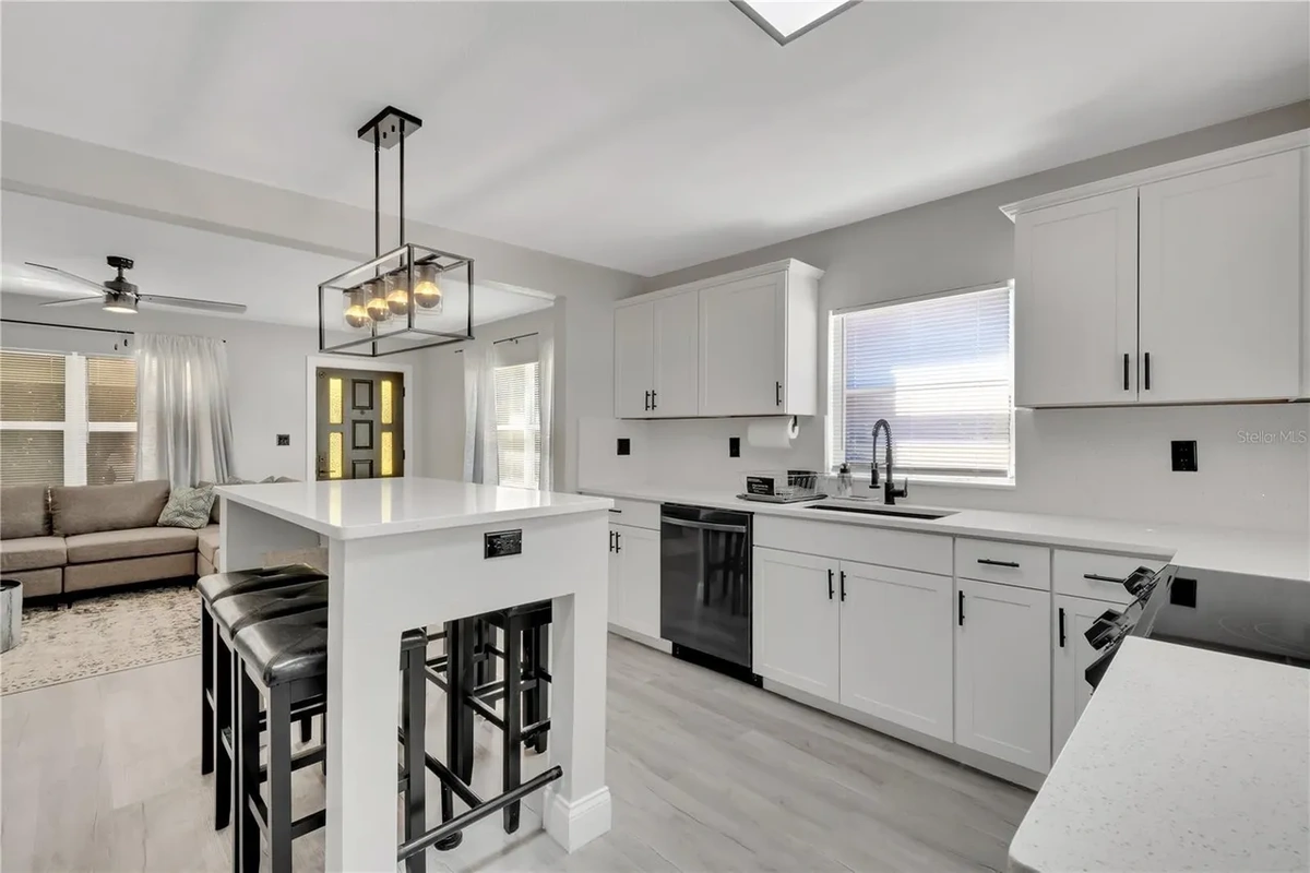 Open concept remodeled Lakeland kitchen with a white island, bar stools, and a view into the living room by Guy A Remodeling