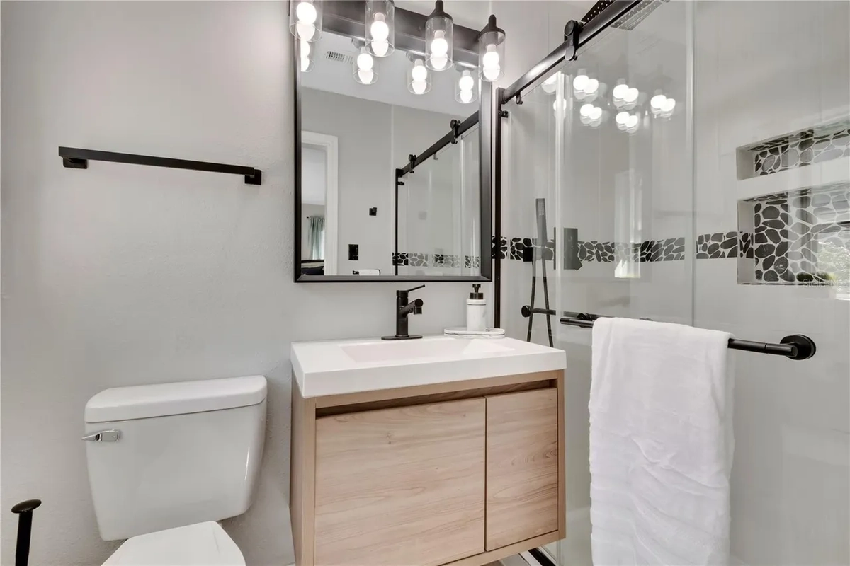 Remodeled Lakeland bathroom with a floating wood vanity, a glass shower, and a large framed mirror by Guy A Remodeling