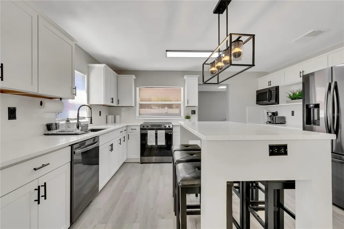 Finished open concept Lakeland kitchen with white cabinets, a black island, and quartz counters