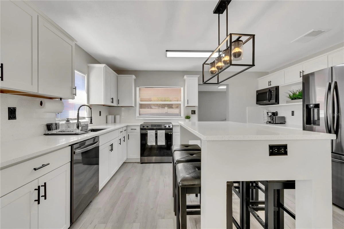 Remodeled Lakeland kitchen with white cabinets, quartz counters, and a black framed pendant light by Guy A Remodeling