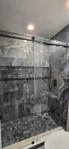 The finished walk in shower with onyx look porcelain, a hexagon mosaic floor, a linear drain, and a handheld on a slide bar