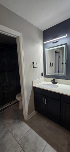 The new vanity with a lit mirror on a navy accent wall, with the finished shower visible through the doorway