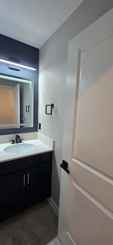 The new vanity with a matte black faucet, an LED light bar, and a lit mirror beside a matte black door lever