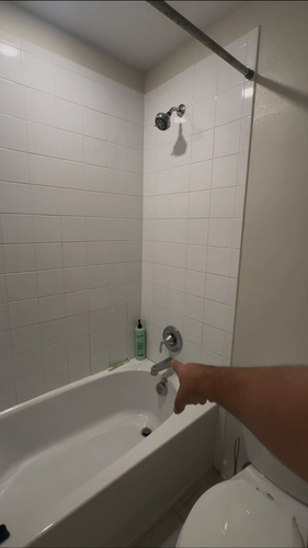 The Kissimmee bathroom before the remodel, with a white tub and shower combo, small square tile, and a curtain rod