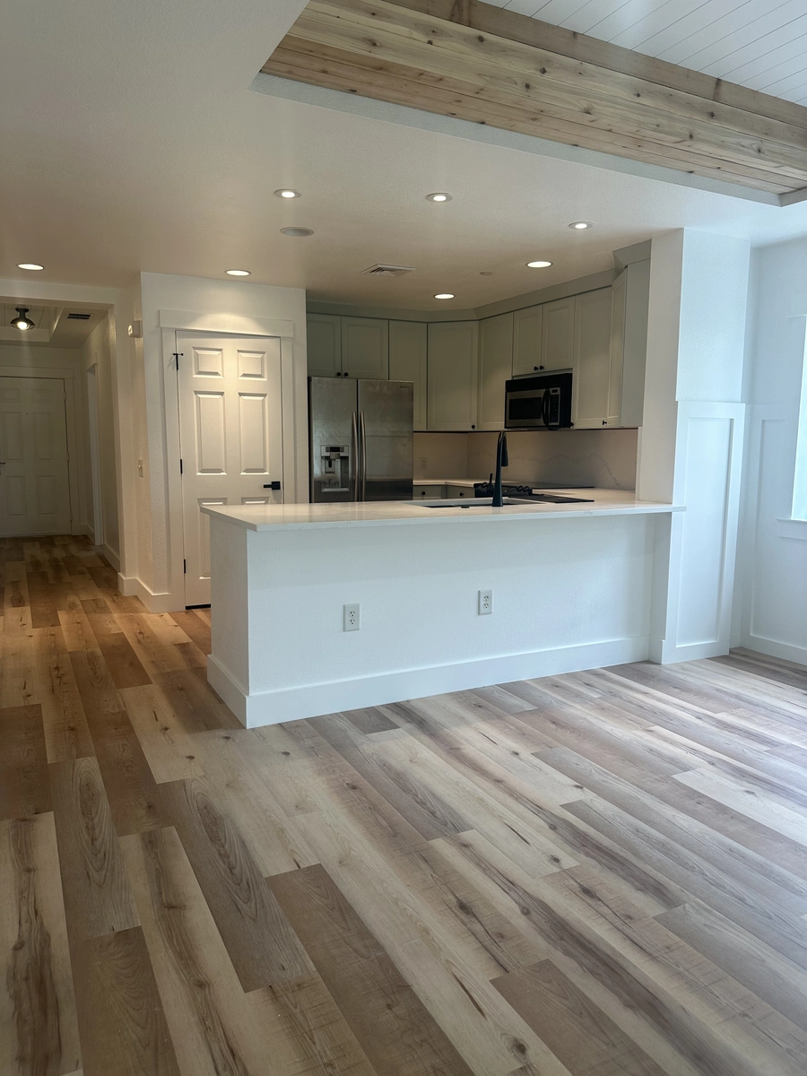 Remodeled kitchen near Celebration with a long peninsula, light cabinets, and wide plank wood flooring by Guy A Remodeling