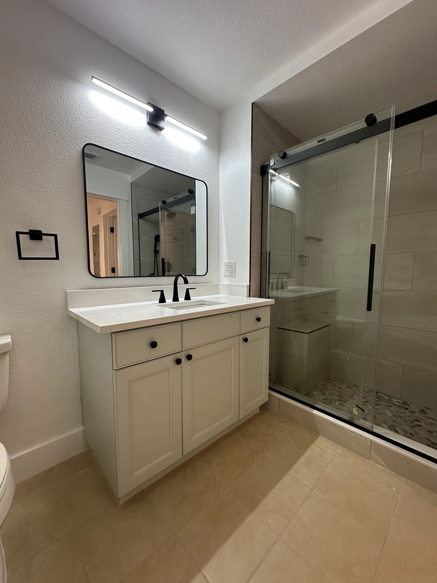 Remodeled bathroom near Celebration with a sliding glass shower door, a shaker vanity, and a black framed mirror by Guy A Remodeling