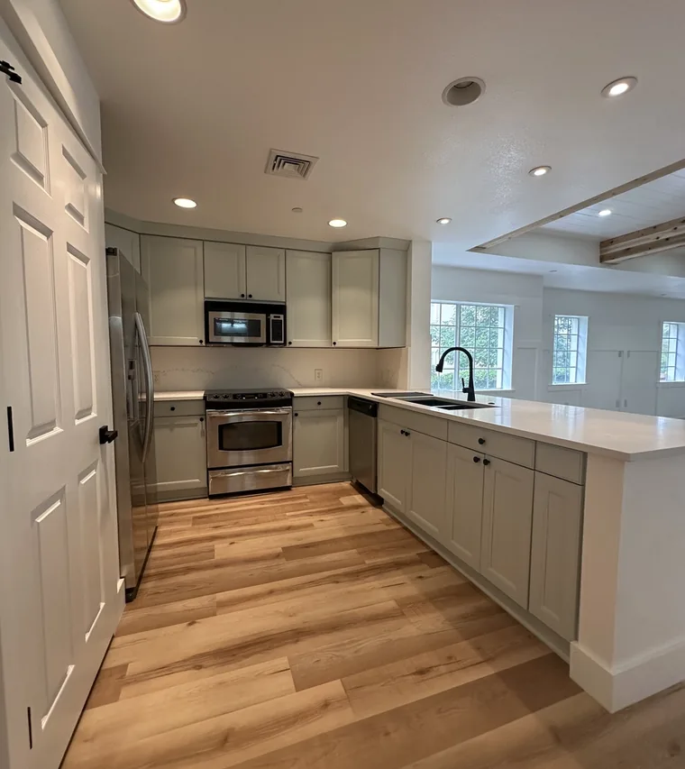 Remodeled kitchen near Celebration with light shaker cabinets, quartz counters, and wide plank wood flooring by Guy A Remodeling