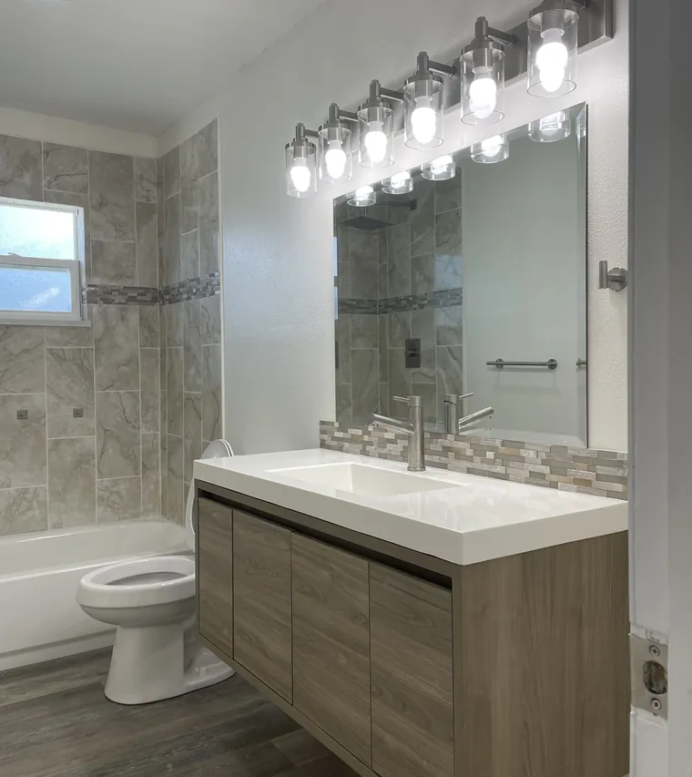 Remodeled Lakeland bathroom with a floating wood vanity, a tiled tub surround, and a wide lighted mirror by Guy A Remodeling
