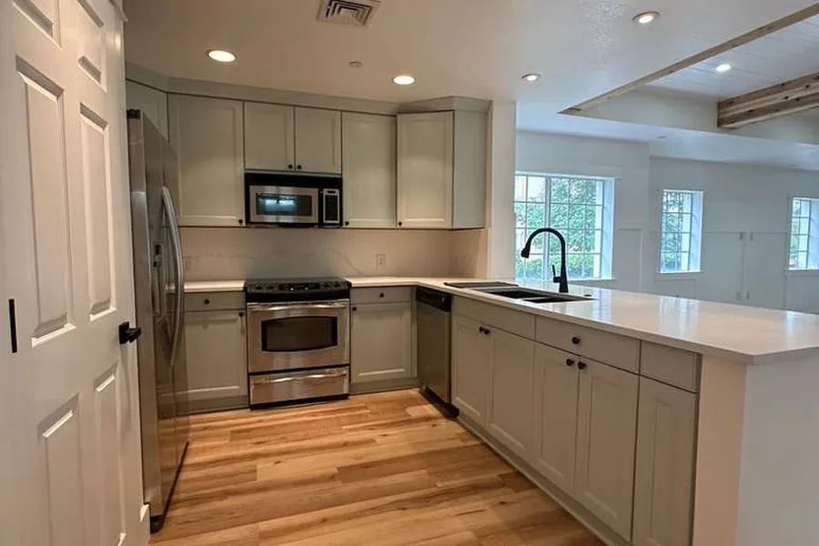 The same kitchen after remodeling with light cabinets, quartz counters, and wide plank wood flooring