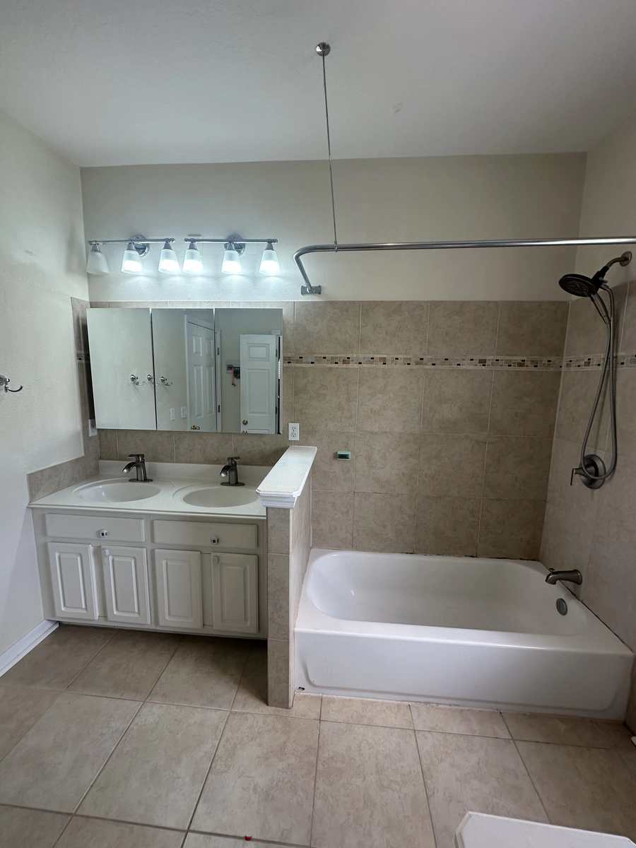 Celebration bathroom before the upgrade with a standard alcove tub, a curtain rod, and beige tile